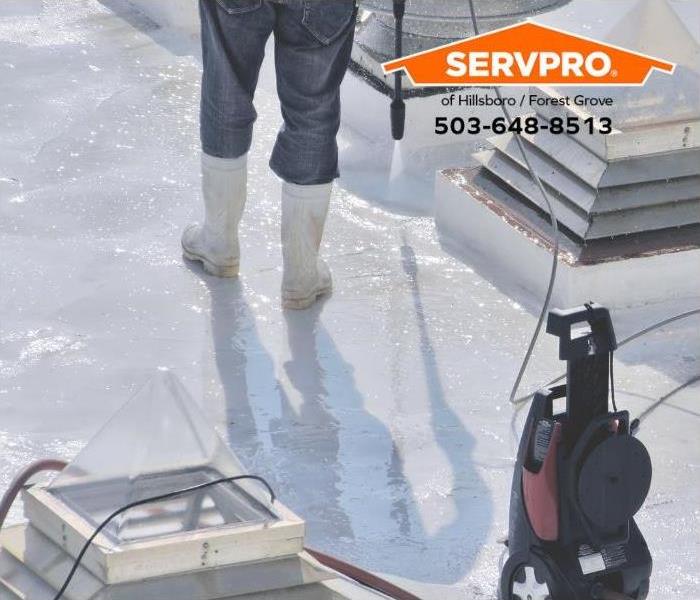 A person is power washing a commercial roof to check for drainage problems.